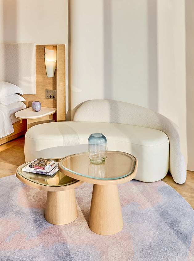 A small modern white sofa next to a wooden table next to the bed at the Corniche Junior Suite.