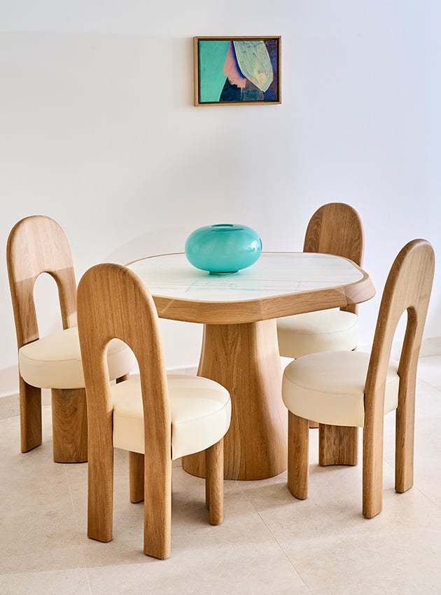 Wooden table with a turquoise vase in the centre and four wooden chairs.