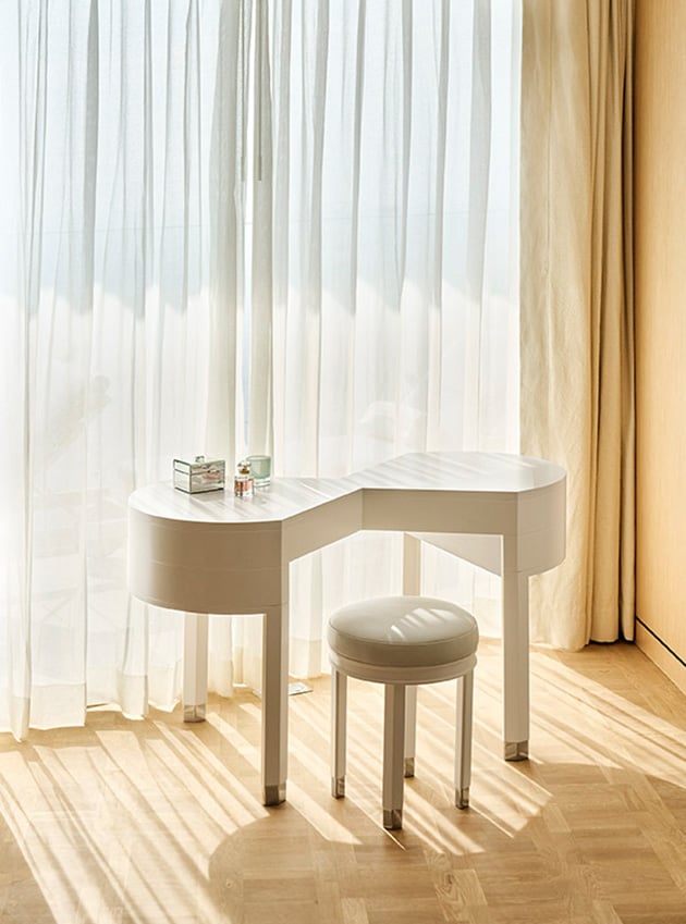 A small white table with a small white stool next to white curtains.