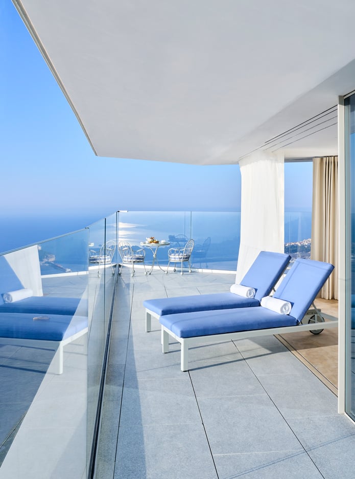Two blue sun loungers on a terrace of a room with a sea view.