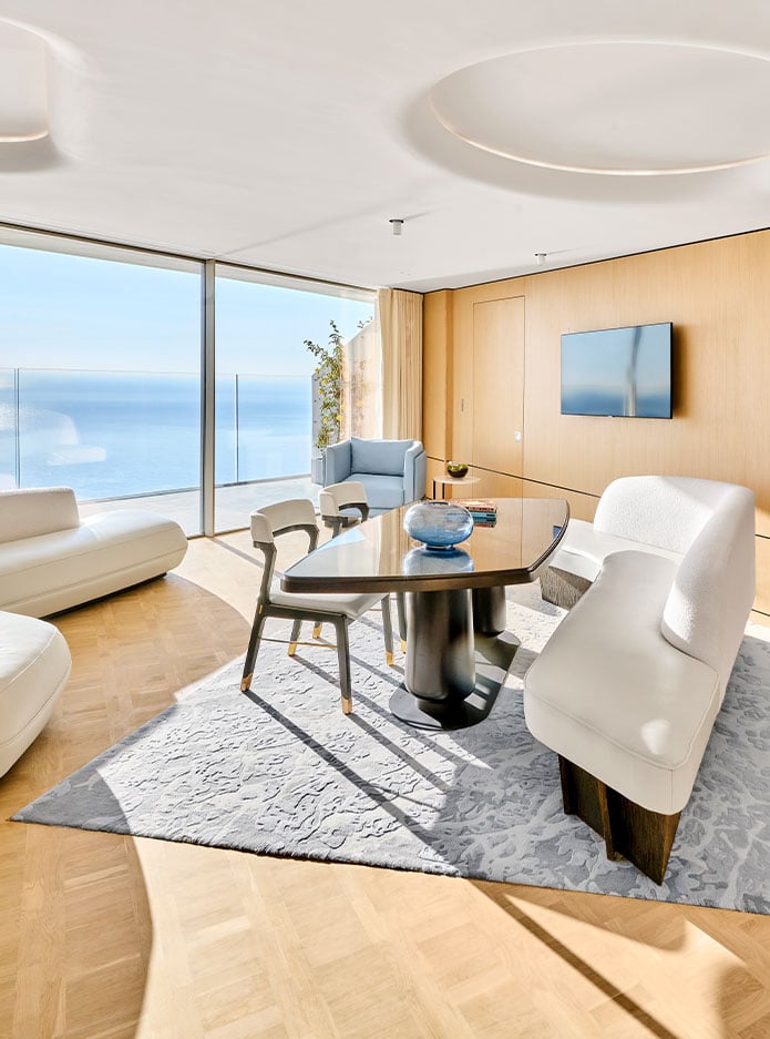 A spacious room with two large white sofas and a table facing the sea at the Riviera Suite.