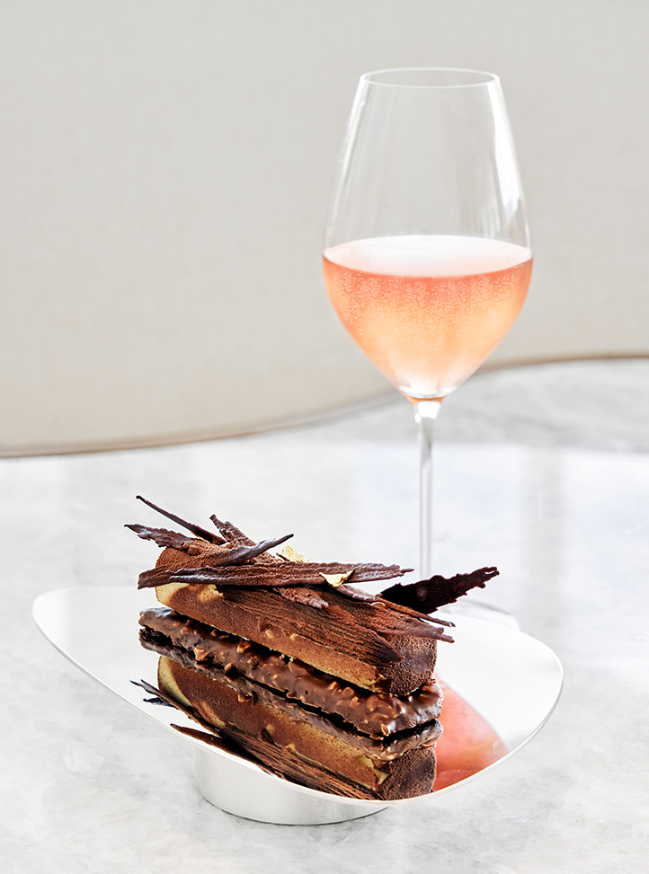 Chocolate cake on a plate with a glass of Champagne Rosé on the side.