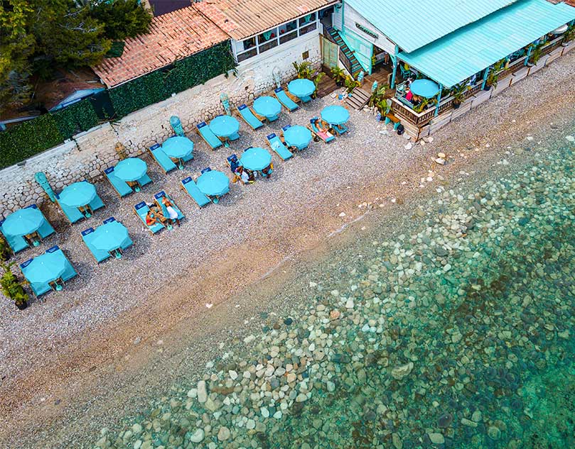 The sea and the coast full of sunbeds and blue umbrellas.