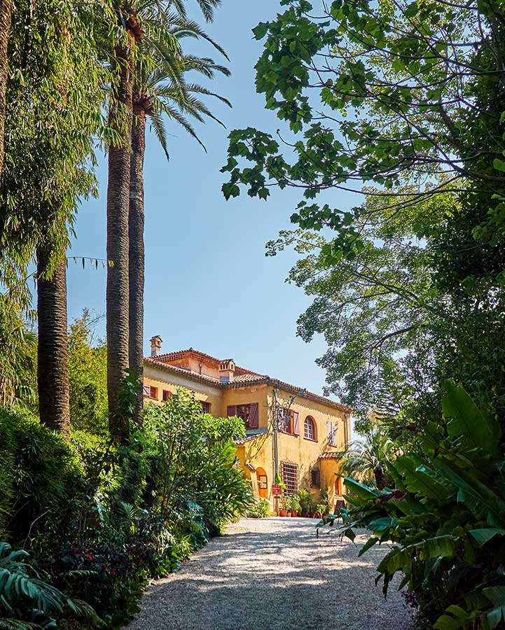 A path with trees with a big house in the background.