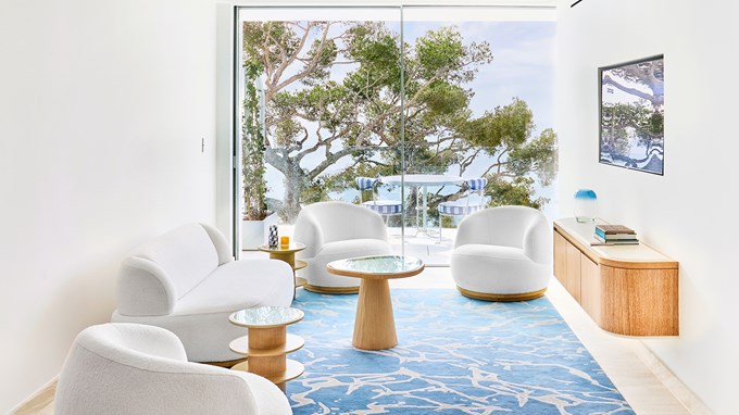 A living room area with white armchairs and coffee table, with a terrace with chairs and table in the background.