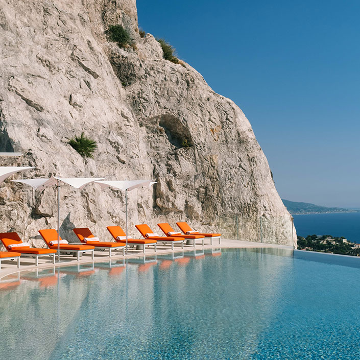 View of the swimming pool, with orange sunbeds and white umbrellas in a relaxing atmosphere.