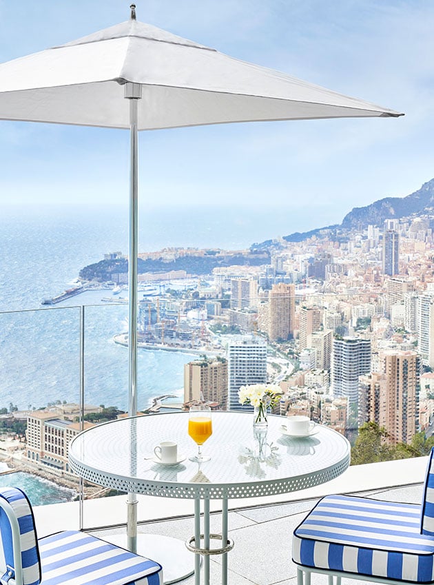 A table with breakfast and two chairs near an umbrella facing the sea.