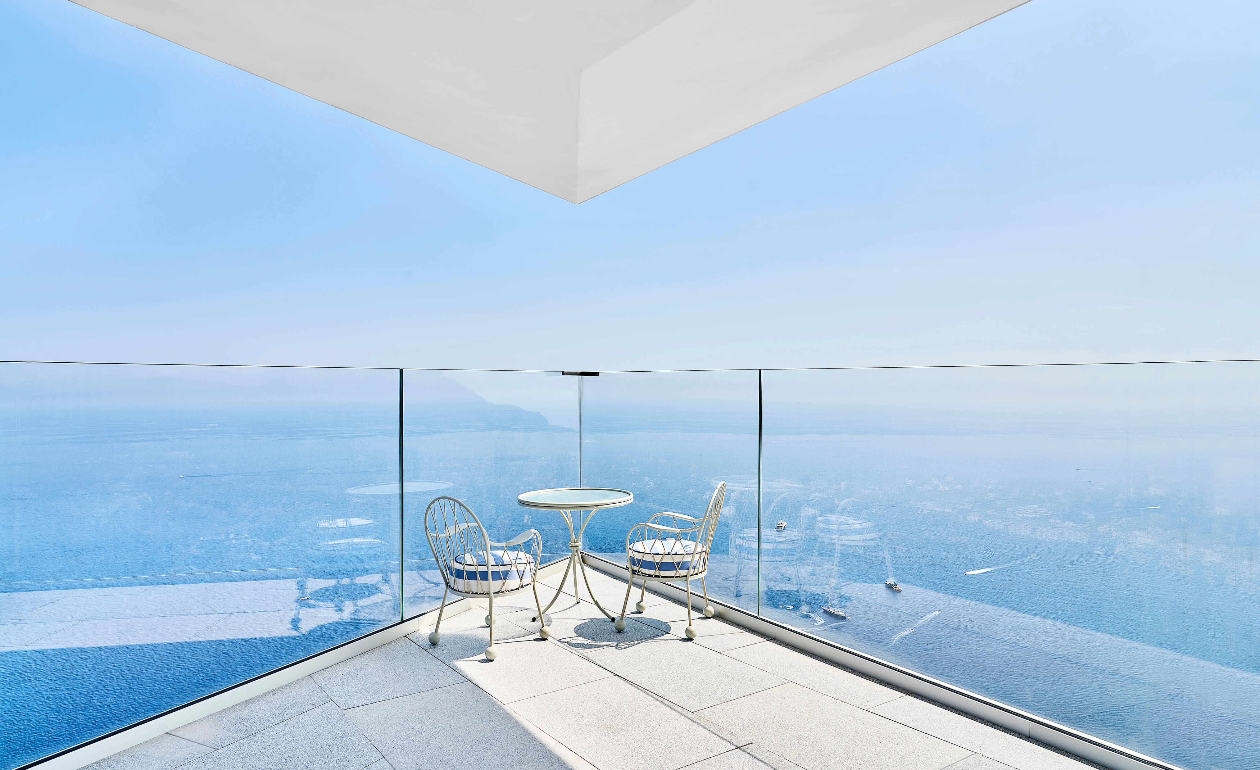 Two chairs and a round table on a terrace with a sea view.