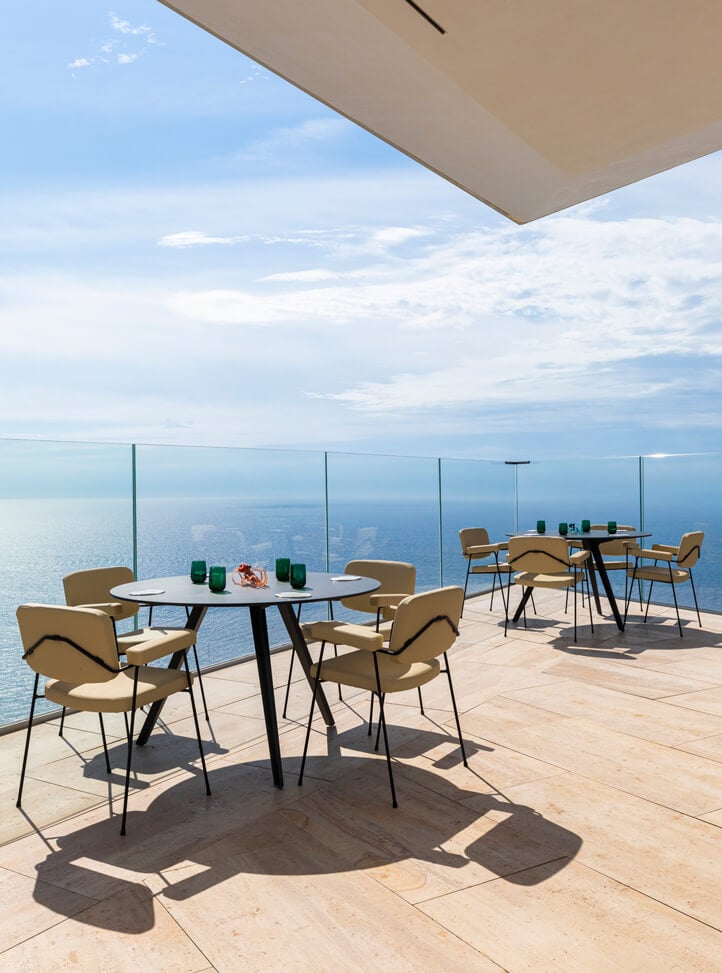 Two round tables with yellow chairs on the terrace overlooking the sea and the blue sky.