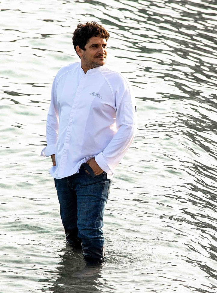 A man in a white shirt and jeans standing in the sea.