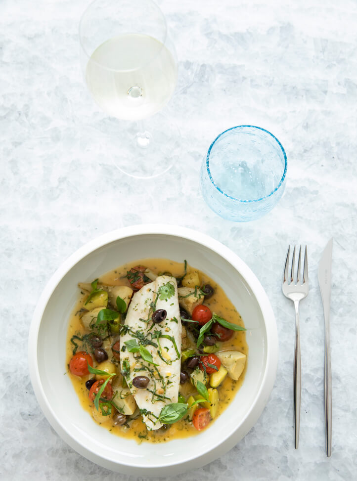 A white plate with food next to a fork, knife, and glass of wine.