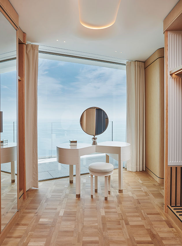 The Grand Sea View Suite walk-in dressing room features a chic white dressing table with a view of the sea, surrounded by the wooden wardrobes