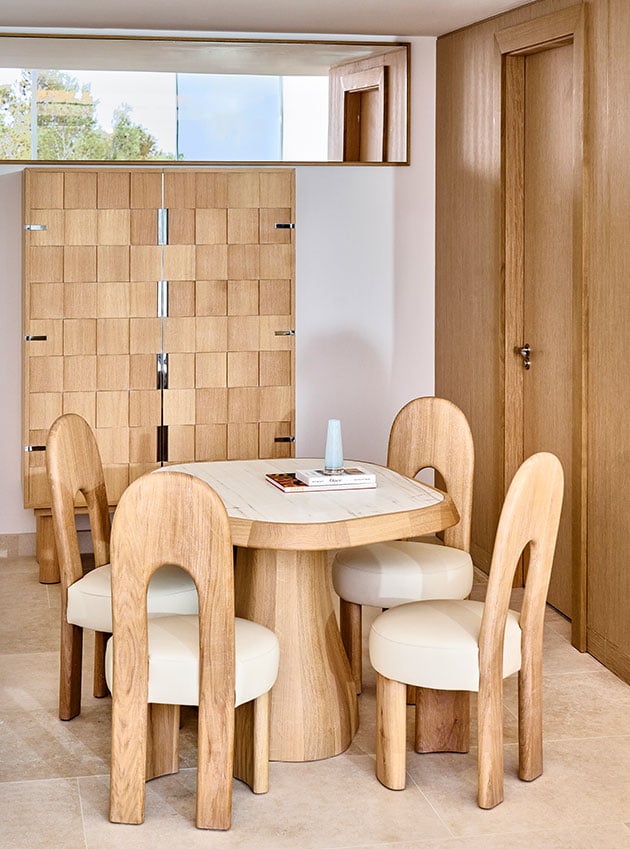 Wooden table with a turquoise vase in the centre and four wooden chairs.