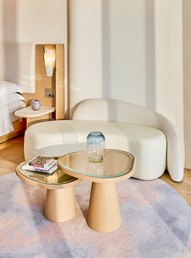 A small modern white sofa next to a wooden table next to the bed at the Corniche Junior Suite.