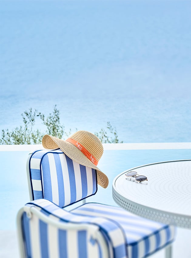 White and blue striped chair with a straw hat hanging from it at the terrace.