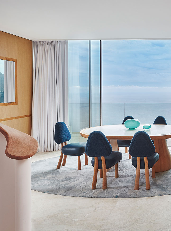 La table à manger de la Grande Suite Duplex Azur avec des chaises bleu foncé autour et une grande baie vitrée avec vue sur la mer.