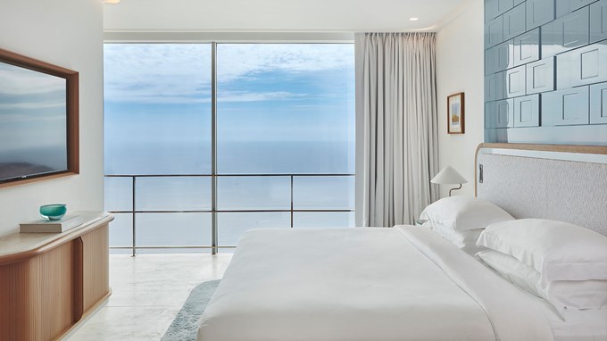 La chambre de la Grande Suite Duplex Azur avec le lit double, la TV au mur, et la terrasse avec vue sur la mer en fond.