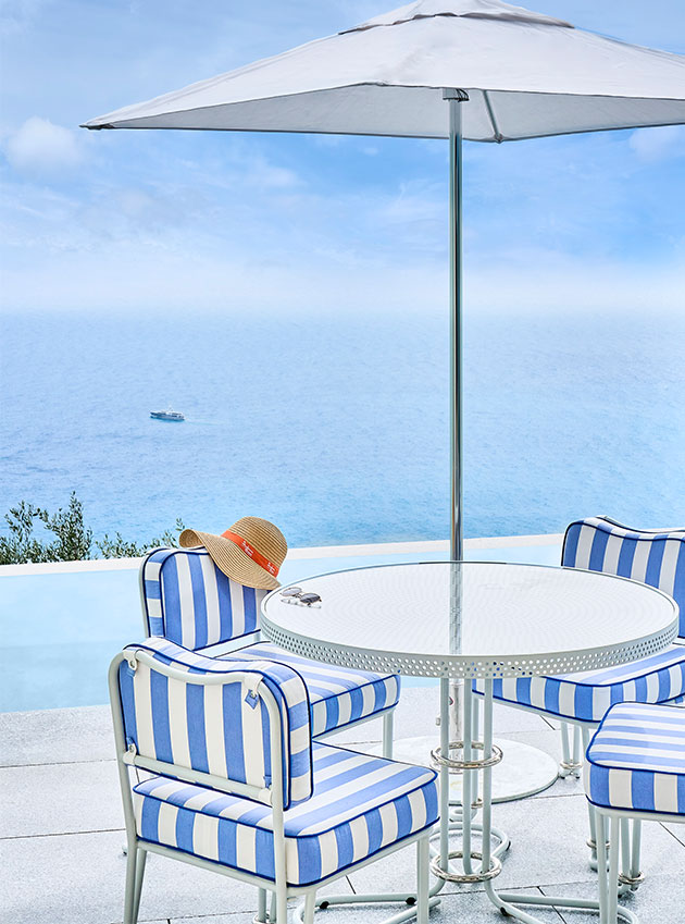 A round table, four white and blue striped chairs, and an umbrella by the infinity pool.