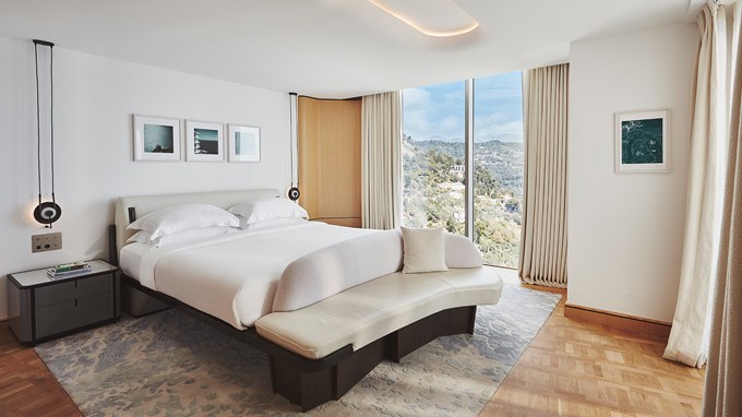 A bedroom with a large bed, table nightstands and a large window with a view on the Riviera.
