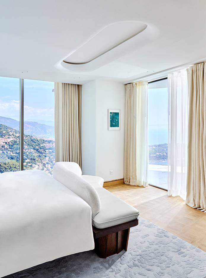 The end of the bed with two glass walls overlooking the mountainous coast and the sea.