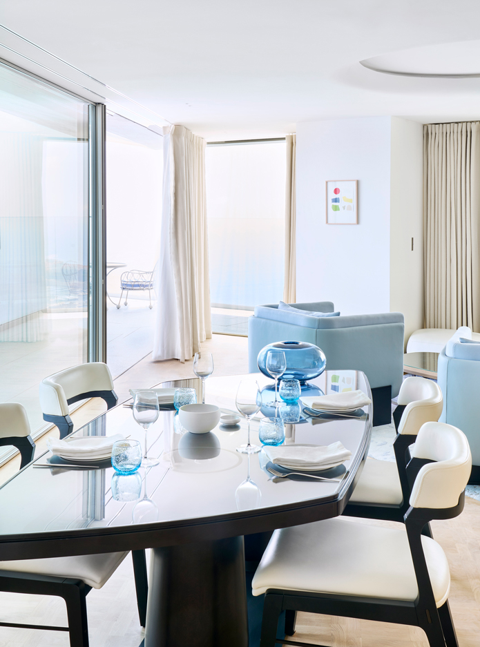 A long black table with white chairs and blue armchairs in the background.