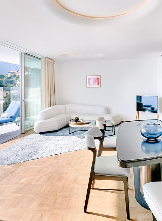 A black table in a room with high chairs, a sofa in the background with a television and an open terrace overlooking the sea.