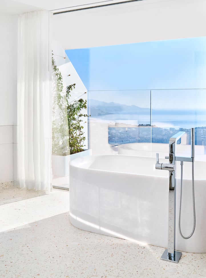 White bathtub next to a glass wall with a view of the sea.
