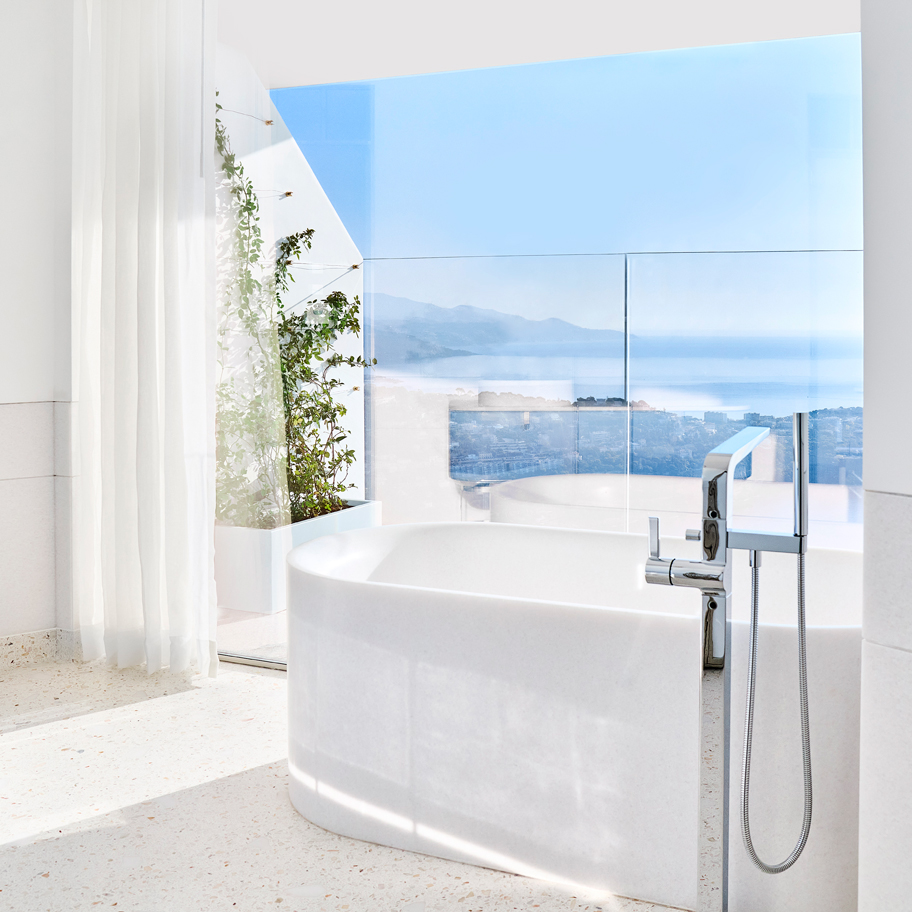 A comfortable bathtub next to a terrace with a creeper plant and the blue sky in the background.