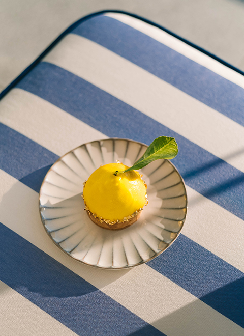 A lemon tart in the shape of a lemon cut in half, on a blue and white striped tablecloth.