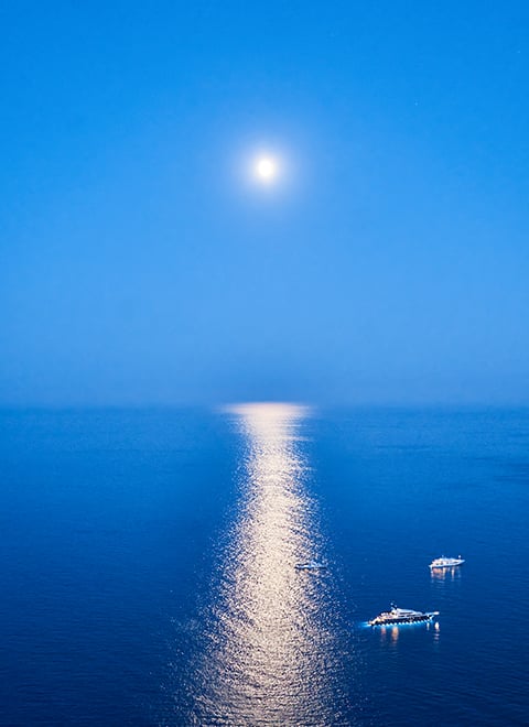 Two yachts on the sea with the sun above.