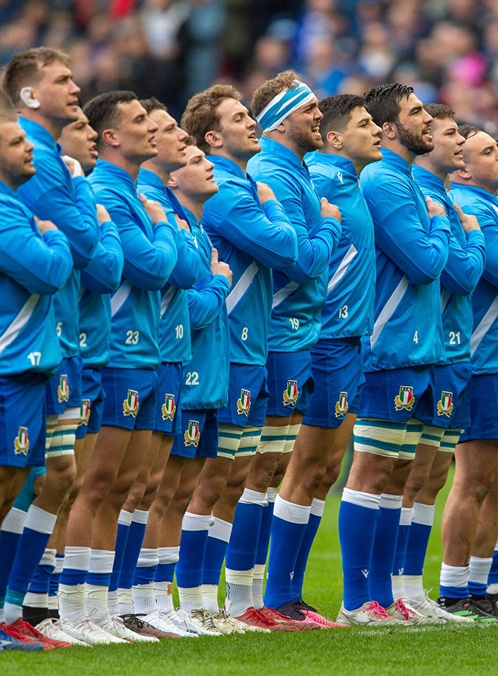 A line of rugby players dressed in a blue kit singing the National Anthem