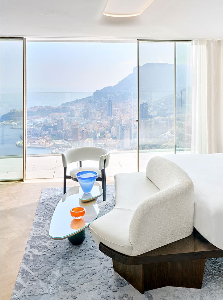 A white sofa at the end of the bed in a room with huge views of the coast.