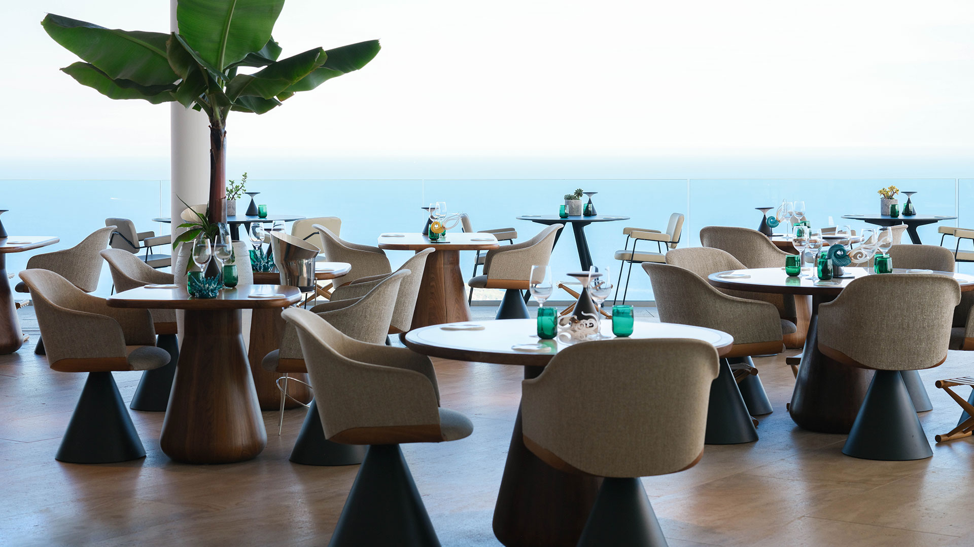 Beige dining chairs around wooden dining tables overlooking the sea at Ceto