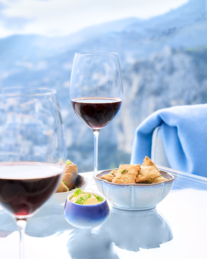 2 glasses of red wine on blue table with selection of bar snacks
