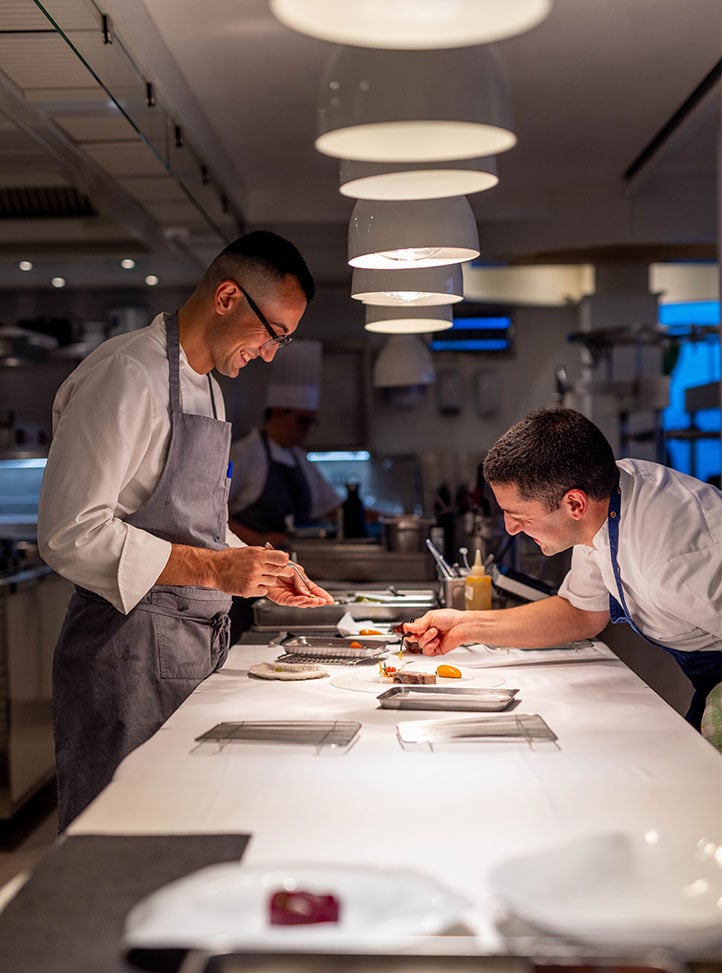 Cette image dans les cuisine du restaurant gastronomique Ceto. Deux chefs cuisinent et sourient lors d'un moment convivial. This picture in the kitchen of the gourmet restaurant Ceto. Two chefs are cooking and smiling during a friendly moment.