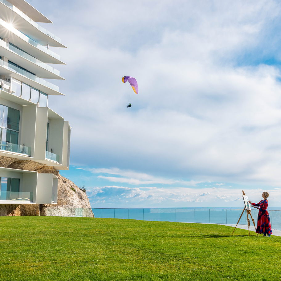 femme qui peint sur la pelouse face à l'hôtel avec un parapente dans le ciel - woman painting on the lawn in front of the hotel with a paraglider in the sky
