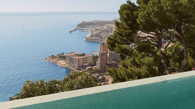 Vue panoramique d'une ville côtière avec de hauts bâtiments au bord de la mer, observée depuis une piscine à débordement et encadrée par des arbres.