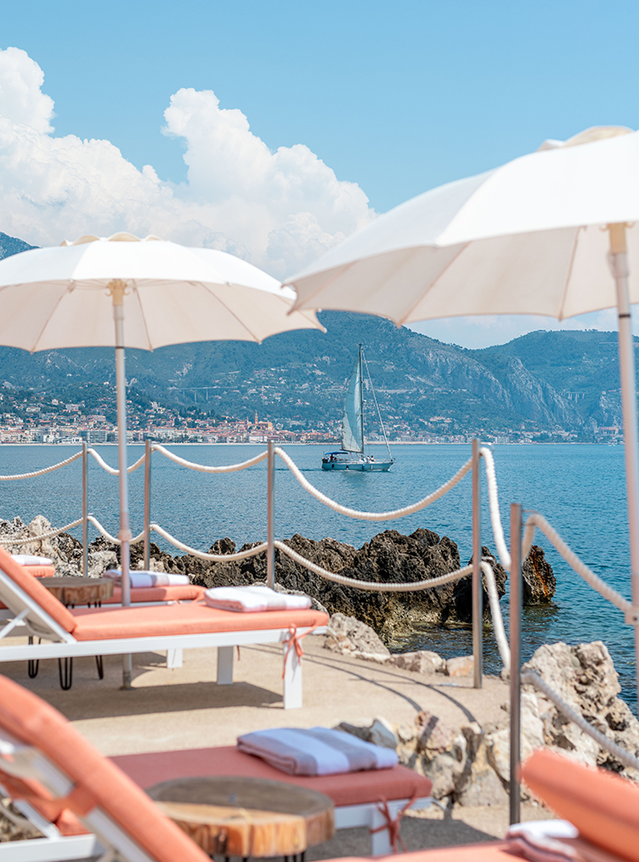 Coral sun loungers at Maybourne La Plage with a view of a boat on the sea and the coastline in the background.