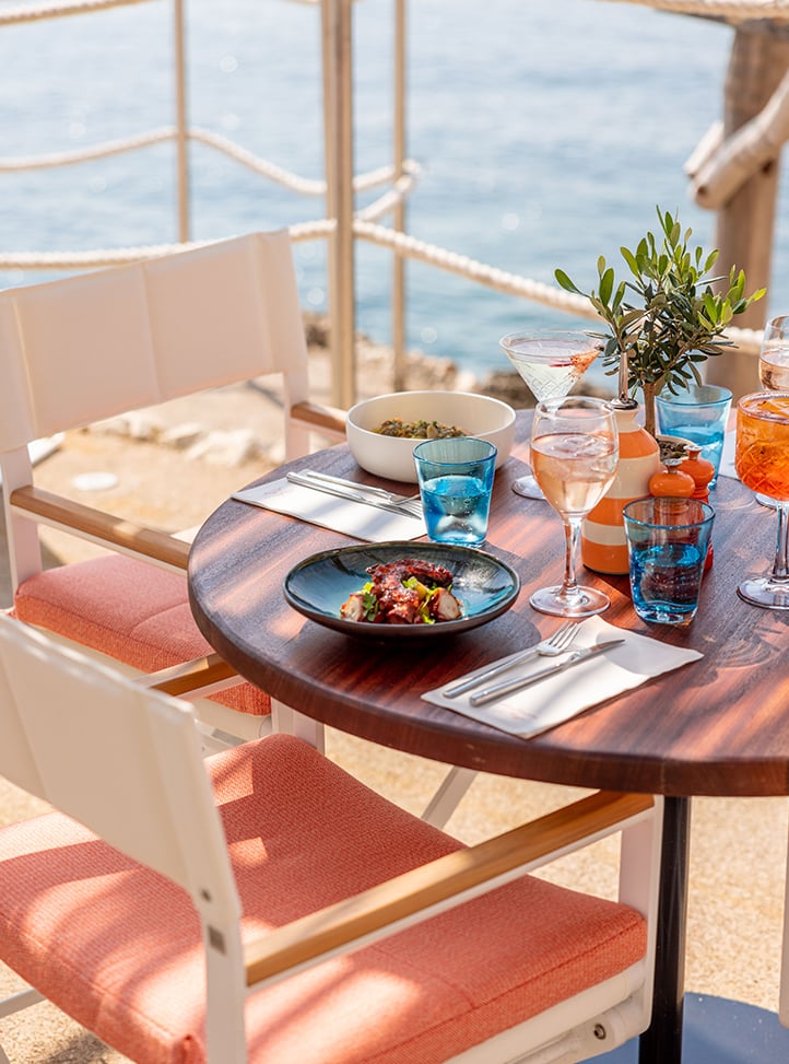 Colourful dishes, cutlery and glassware on a table at Maybourne La Plage with a view on the sea.