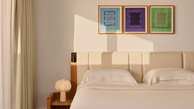 Detail view of a softly lit bed with textured headboard and three abstract prints above.