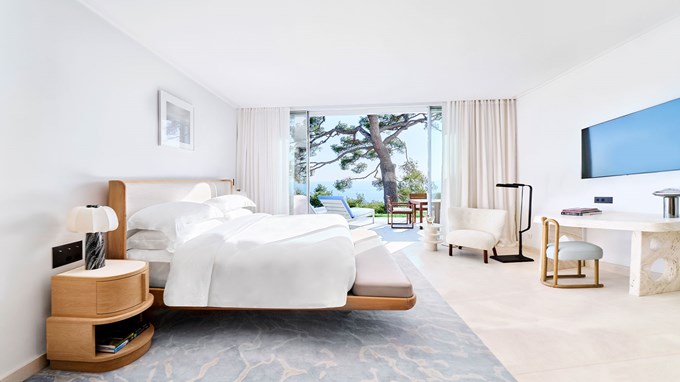 ChatGPT said: Bright and spacious studio with a king bed, modern furnishings, and floor-to-ceiling glass doors opening onto a private terrace with sea views framed by pine trees.