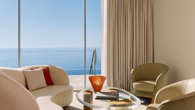 Curved white sofa and lounge chairs beside window with ocean backdrop.