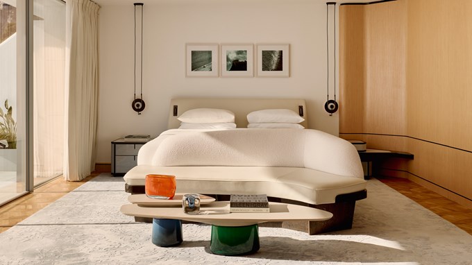 Chambre spacieuse avec lit double, canapé incurvé en tissu clair, table basse design et trois cadres photo au mur dans un décor moderne et lumineux.