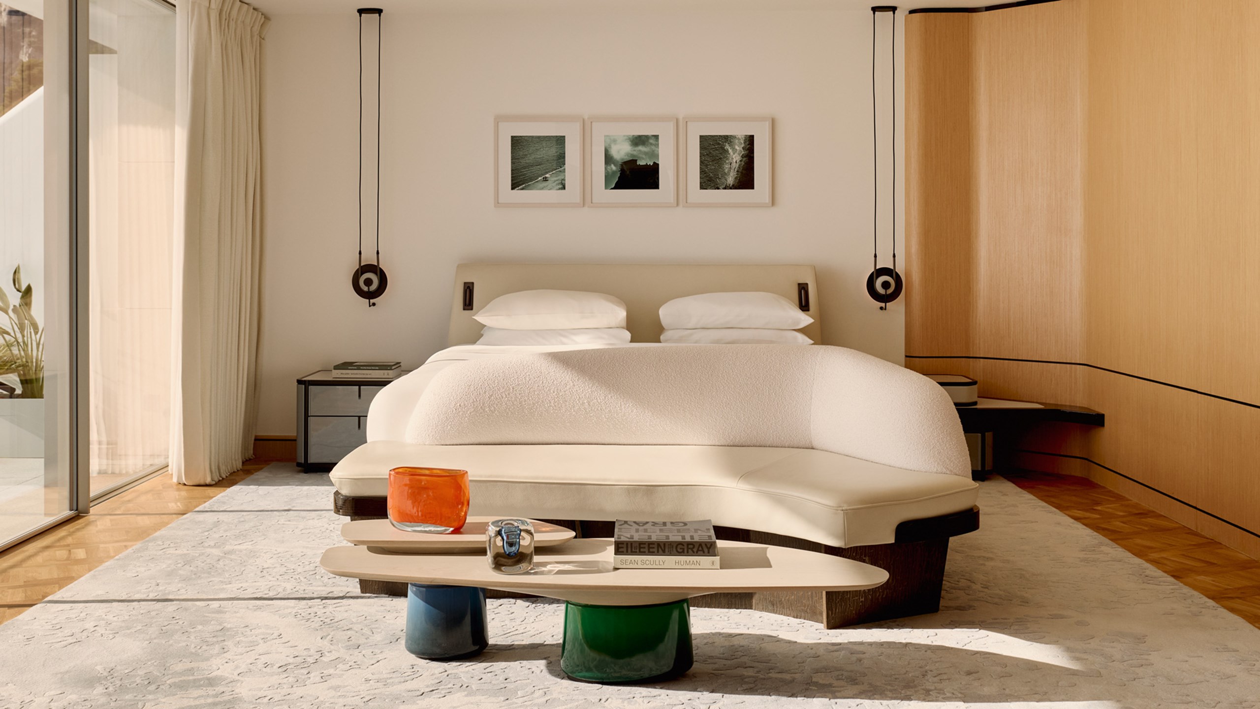 Serene bedroom with sculptural furnishings and sea-facing glass doors.