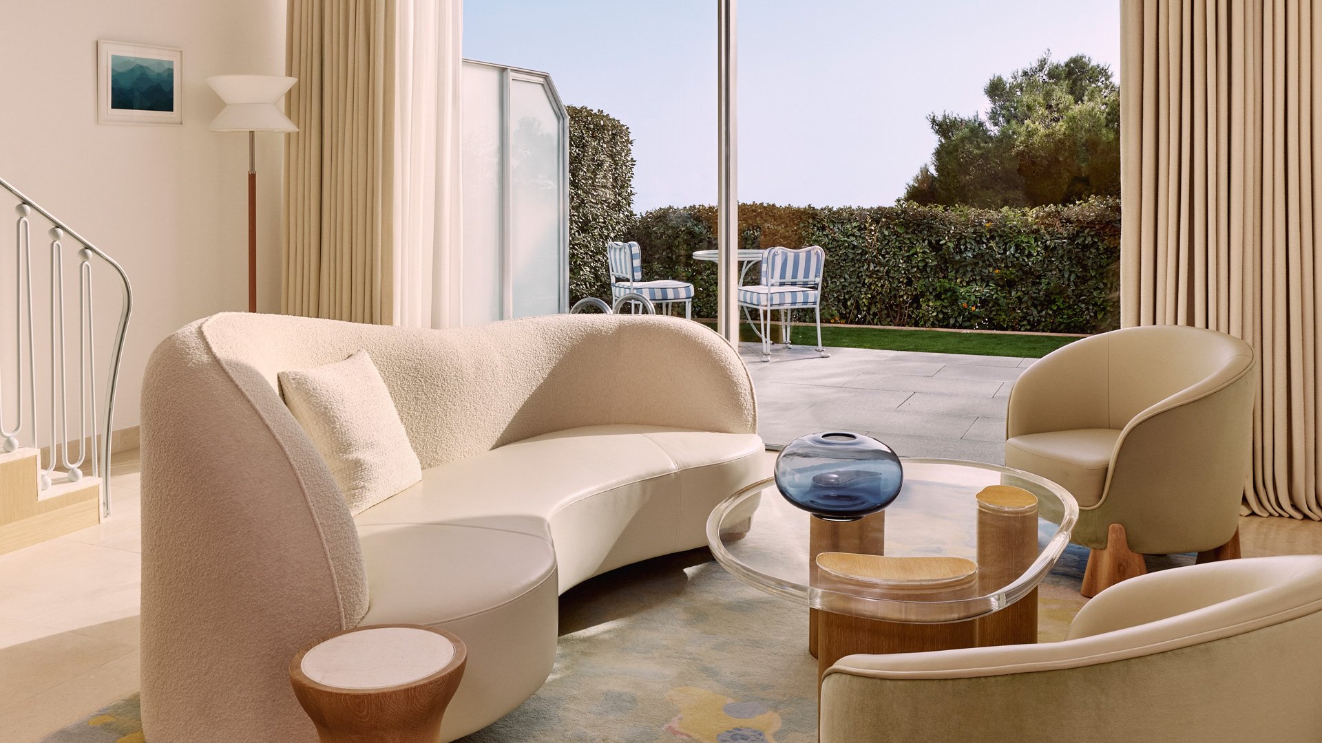 Soft-toned living room with curved sofa and colourful rug, opening onto a private garden terrace.
