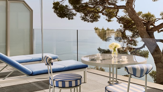 Private terrace with striped chairs, sun loungers, and sea views through a glass balustrade.