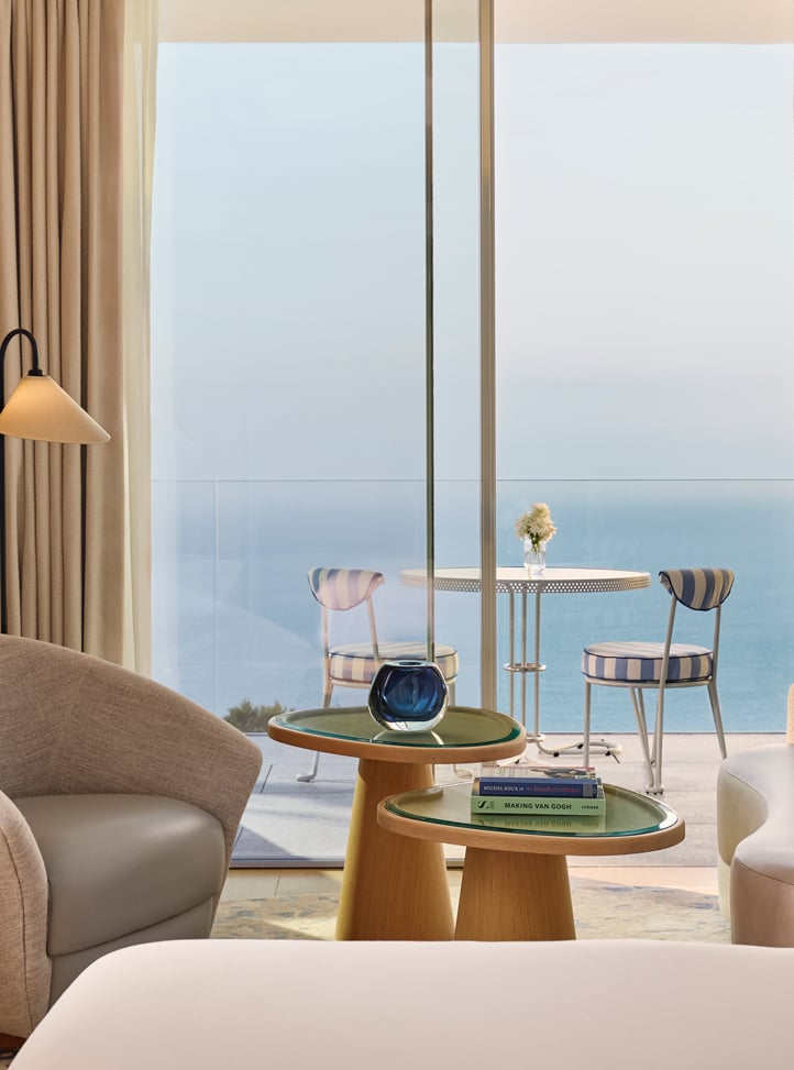 Curved sofa and two armchairs in front of balcony overlooking the sea through full-length windows.