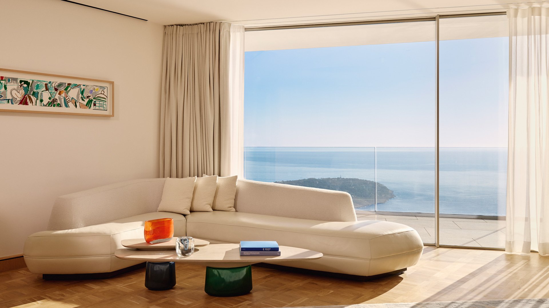 Cream curved sofa in front of a floor-to-ceiling window with sweeping ocean views.