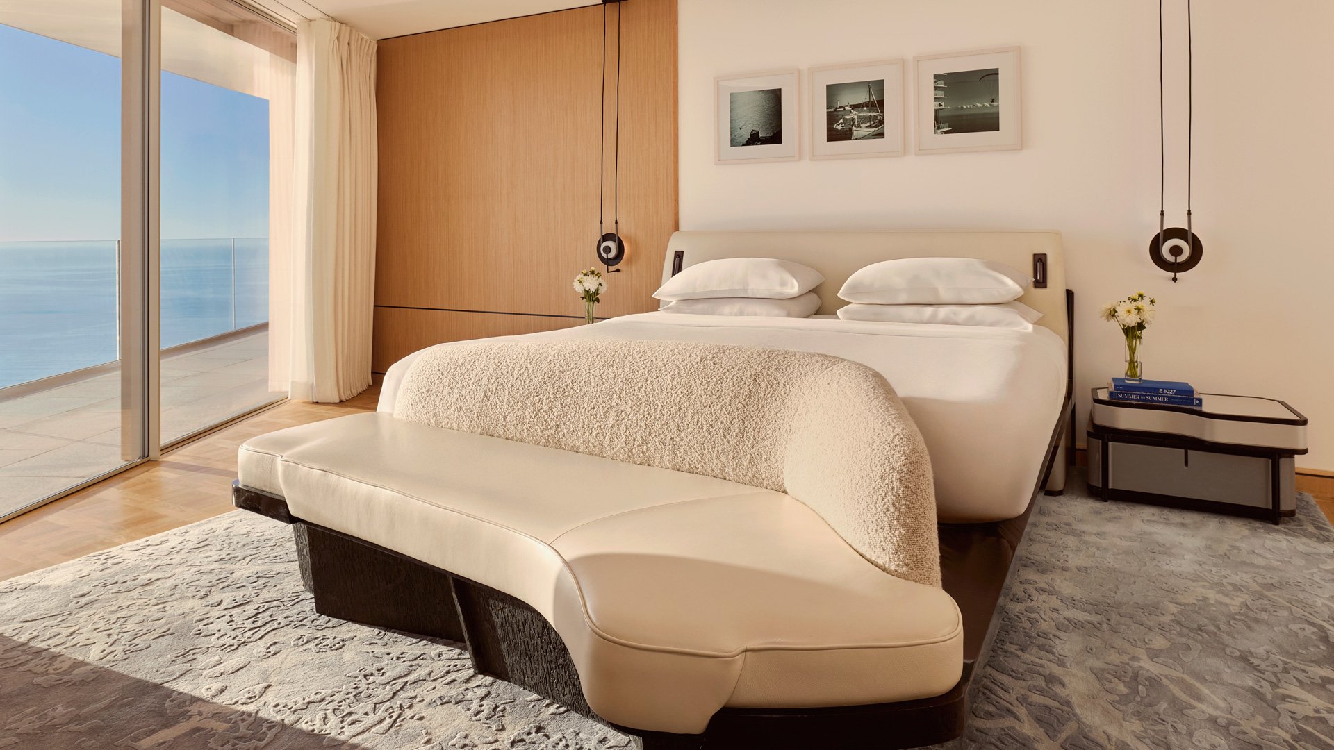 Elegant bedroom with textured bench and large windows opening to a sea-view balcony.