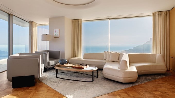 Spacious, modern living room with curved white sofa, glass coffee table, and panoramic sea views through floor-to-ceiling windows.